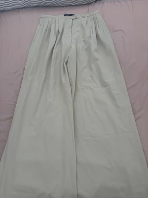 Vida beige linnebyxor  - Superfina vida linnebyxor i beige från H&M. Byxorna har hög midja, pressveck och knäppning fram med knapp och dragkedja. Perfekta för en chill och stilren look, och materialet känns lätt och luftigt. Snygga att matcha med crop top eller skjorta.