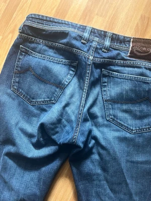 Mörkblå jeans från Jacob Cohen - Snygga mörkblå jeans från Jacob Cohen med klassisk femficksdesign och raka ben. Jeansen har tydliga kontrastsömmar och en läderpatch med logga bak i midjan. Tillverkade i mjukt denimtyg som ger en skön passform.