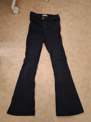Svarta flared jeans med high waist  - Är 154cm Snygga svarta jeans med utsvängda ben och hög midja. Klassisk femficksmodell med dragkedja och knapp framtill. Perfekta för dig som gillar retrostil och vill ha ett par jeans som sticker ut lite extra. Finns att litet problem. Under det högra låret hade jag sytt ett litet hål. 