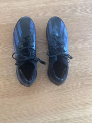 Svarta adidas crazy fast elite fotbollsskor  - Säljer ett par snygga fotbollsskor från Adidas i svart med lila detaljer och klassiska ränder. Skorna har ett nypris runt 3000 kr. Skorna har snörning och dobbar i plast för bra grepp på planen. Ovandelen är i syntetmaterial och designen är smal och sportig, perfekt för dig som vill ha kontroll och fart. Hör av dig med prisförslag 