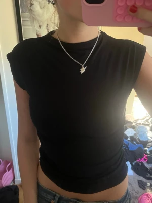 Svart croppad topp - En enkel svart croppad topp med rund hals och ärmlös design. Perfekt till jeans eller kjol för en clean och stilren look. Mjuk och stretchig känsla.