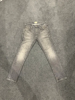 Grå slim fit jeans med slitningar - Snygga grå slim fit jeans med slitningar och tvättade detaljer på låren och knäna. Klassisk femficksmodell med dragkedjegylf och bälteshällor. Perfekta för en avslappnad och trendig look.