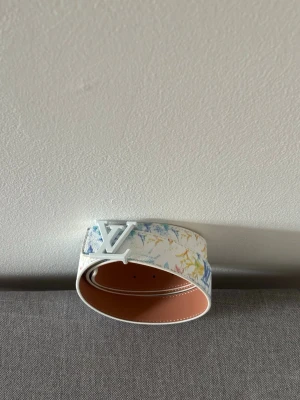 vitt bälte med färgstänk L - bälte i vitt med färgstänk i blått, gult och rött. Snyggt -spänne i vitfärg och exklusiv känsla.  och har en modern, trendig look som sticker ut. OBS: ingen förpackning/box.