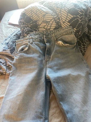 Ljusblåa baggy jeans i denim - Säljer ett par ljusblåa baggy jeans i klassisk denim med raka ben och fem fickor. Jeansen har en avslappnad passform och mid waist, perfekta för en chill och trendig look. Inget synligt märke på byxorna.