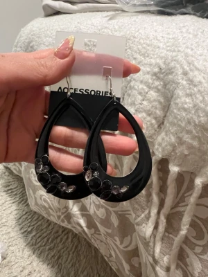 Svarta droppformade örhängen - Stilrena svarta örhängen i droppform från Accessories. De har dekorativa svarta pärlor och silvriga detaljer längst ner på varje örhänge. Perfekta för att ge din look en cool touch. Materialet är lätt och känns bekvämt att bära.
