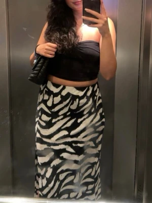Zebramönstrad långkjol i svartvitt - Snygg långkjol med zebramönster i svart och vitt. Kjolen har en rak och flowy passform som ger en cool och trendig look. Perfekt att styla med crop top eller t-shirt. Materialet känns mjukt och följsamt mot kroppen.