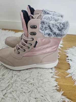 Rosa vinterstövlar med fuskpäls - Snygga rosa vinterstövlar från Livergy med gråvit fuskpäls upptill och snörning framtill. Stövlarna har en kombination av matt och glansigt material samt robust vit sula. Perfekta för kalla dagar när du vill hålla stilen och värmen.