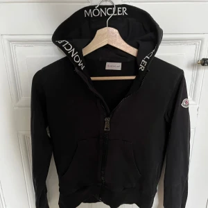 Moncler hoodie - Hej! Jag säljer denna sjukt snygga och stilrena svarta hoodien från Moncler!😁 Den har en logga på vänstra ärmen och ”Moncler” text på kanten på insidan längs dragkedjan och luvan. Såklart äkta! Hör av dig om frågor!😁🤩