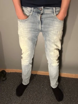 Replay anbass slitna jeans - Säljer ett par ljusblå skinny jeans från replay med slitningar och distressed detaljer på låren och knäna. Jeansen har klassisk femficksdesign, dragkedjegylf och är tillverkade i stretchigt denim för en bekväm passform.