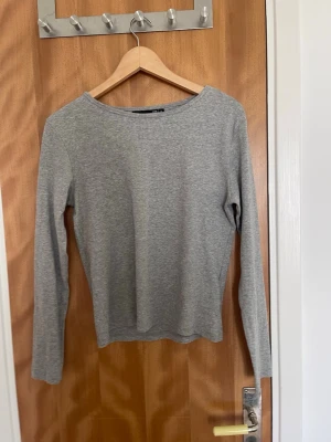 Grå långärmad topp i bomull - En enkel och stilren grå långärmad topp med rund halsringning. Tillverkad i mjuk bomull, perfekt för en avslappnad och clean look. Passformen är normal och toppen är lätt att matcha med olika outfits.