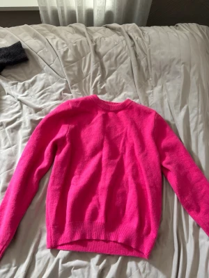 Knallrosa stickad tröja - En snygg och enkel knallrosa stickad tröja med rund halsringning och långa ärmar. Tröjan har ribbade muddar vid ärmslut och nederkant. Perfekt för dig som vill sticka ut med färg i din outfit.