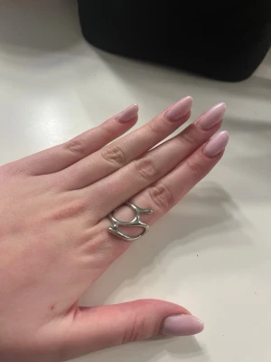 Silvrig abstrakt ring i metall - Cool ring i silvrig metall med en öppen, abstrakt design som ger en modern och unik känsla. Perfekt för dig som gillar statement-smycken och vill sticka ut med din stil. Ringen har en organisk form och passar flera olika fingrar. Köpt utomlands.