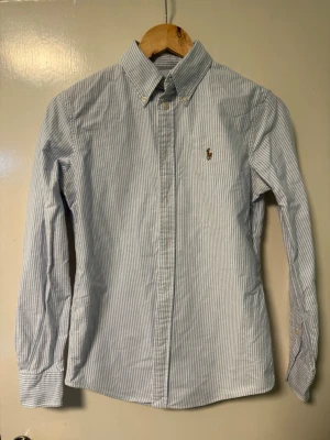 Ralph Lauren skjorta randig - S - Säljer en stilren och snygg blåvit randig skjorta från Ralph Lauren. Storlek S (custom fit). Skjortan är i mycket fint skick och passar utmärkt, både till vardags och mer uppklädda tillfällen.  Har du några frågor? Tveka inte att höra av dig!Allt gott från Deluxe-garderoben