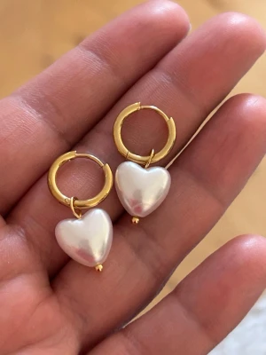 örhängen med hjärtformade pärlor - Snygga örhängen med guldfärgade ringar och hjärtformade vita hjärta pärlor. Perfekta för att ge din look en söt och trendig touch. Passar dig som gillar unika accessoarer med lite extra glans.