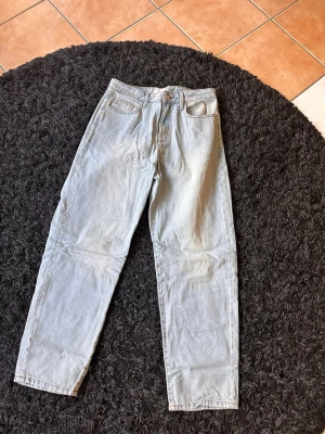 Ljusblå raka jeans i denim - Säljer ett par ljusblå jeans i klassisk rak modell med fem fickor och hög midja. Jeansen är tillverkade i denim och har en tidlös look som passar till det mesta. Perfekta för dig som gillar en clean och enkel stil.