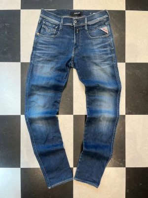 Blå Replay jeans Anbass - Snygga blå jeans från Replay med klassisk femficksmodell och coola slitningar framtill. Jeansen har raka ben, tydliga kontrastsömmar och Replay-logga på fickan. Tillverkade i bomull med en skön passform som funkar till det mesta.