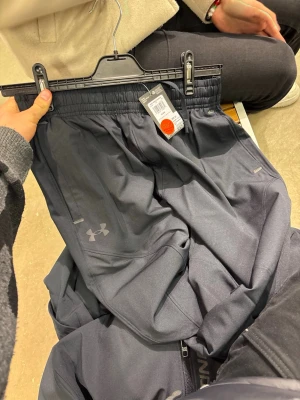 Svart träningsset från Under Armour - Snyggt svart träningsset från Under Armour med byxor och långärmad tröja. Setet har diskreta loggor, dragkedja på tröjan och elastisk midja på byxorna. Perfekt för gymmet eller löprundan, tillverkat i ett lätt och funktionellt material.