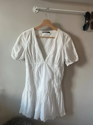  Ny Vit kort klänning med spetsdetaljer - Superfin vit kort klänning från ZARA med v-ringning, korta ärmar och volangkant nertill. Klänningen har spetsdetaljer och är tillverkad i ett lätt bomullstyg som passar perfekt till varmare dagar. Enkel och stilren design med romantiska inslag.
