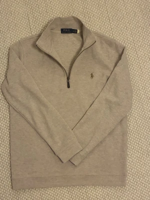 Beige halvzip-tröja från Polo Ralph Lauren - M men passar mer S. Snygg beige långärmad tröja från Polo Ralph Lauren med halv dragkedja och broderad logga på bröstet. Tröjan har hög krage och är tillverkad i mjukt material, perfekt för lager-på-lager-stil.