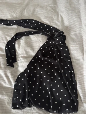 Svart prickig halterneck topp - Säljer en svart halterneck topp med öppen rygg  från h&m med vita prickar och knytband i nacken som aldrig har kommit till användning. 🖤