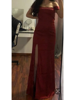 Bal/festklänning - Snygg vinröd långklänning med off shoulder-design och hög slits framtill från Nelly. Klänningen har en figurnära passform. Endast använd i några timmar.