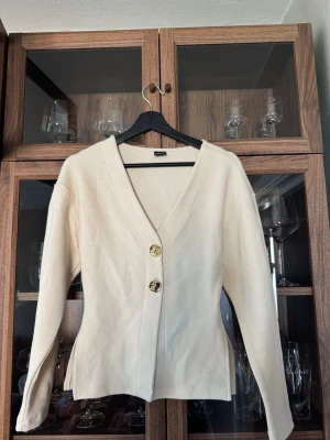 Cream white cardigan - Stilren kräm vit kofta med djup V-ringning och två stora guldfärgade knappar framtill. Koftan har lång ärm, lätt figursydd passform och är tillverkad i ett mjukt mateial. Perfekt att ha antigen som den är eller över en tröja. Köpt på Gina tricot för 499kr och använt 2 gånger🌸