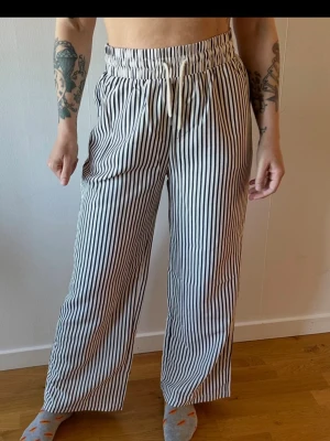 Randiga loungewear-byxor med dragsko - Superbekväma loungewear-byxor i vitt med svarta vertikala ränder. Vida ben och elastisk midja med dragsko för extra komfort. Perfekta för att chilla hemma eller mysa runt i. Luftigt material som känns skönt mot huden.