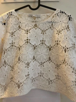 Vit spetsblus från Zara - Superfin vit blus från Zara med stora virkade blommor i spets. Blusen är genombruten och har en lös passform, perfekt att styla över ett linne eller bikini. Rund halsringning och långa ärmar ger en trendig och bohemisk vibe. Har lite smink fläckar runt kragen men man märker inte de.