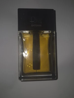 Dior Homme Intense Eau de Parfum - Dior Homme Intense är en lyxig parfym med en elegant, rektangulär glasflaska och svart lock. Doften har en djup gul färg och flaskan har en modern design med tydliga linjer. Perfekt för dig som vill ha en exklusiv och maskulin doft.