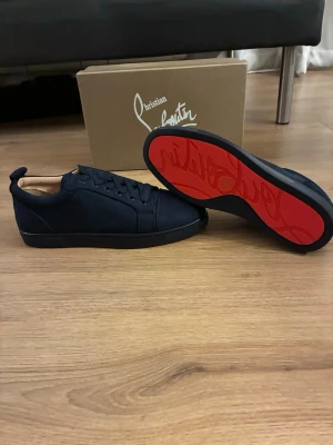 Blåa sneakers från Christian Louboutin - Snygga blåa sneakers från Christian Louboutin med klassisk röd sula och diskret logga. Skorna har en låg profil, rund tå och är tillverkade i ett lyxigt material med svarta skosnören. Perfekt för dig som vill ha en stilren och exklusiv look. Pris går att diskutera 