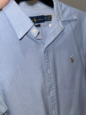 Ralph Lauren Ljusblå skjorta - Klassisk ljusblå skjorta från Ralph Lauren med broderad logga på bröstet. Perfekt för en stilren look och tillverkad i mjuk bomull. Xs och slimfit. Nypris 1800kr. 