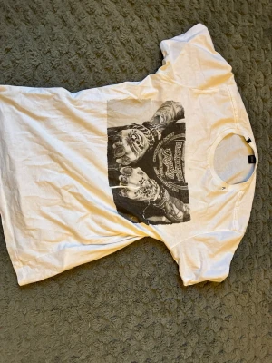 Vit t-shirt med tryck från replay - Vit t-shirt från replay med ett stort svartvitt tryck framtill som föreställer tatuerade händer och text. Klassisk rund hals och korta ärmar. Perfekt för dig som gillar streetstyle och coola motiv.