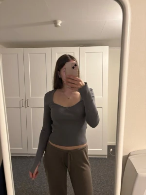 Grå ribbad långärmad topp Gina Tricot - Snygg grå ribbad topp från Gina Tricot med lång ärm och v-ringad hals. Modellen är figurnära och croppad, perfekt till jeans eller kjol. Materialet är mjukt och stretchigt för en bekväm passform.