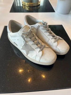 Golden Goose Superstar Sneakers - Säljer mina Golden Goose Superstar sneakers i vitt med klassisk stjärna på sidan. Perfekt blandning av lyx och avslappnad look!  • Storlek: 43 • Skick: Använda men i fint skick – har den typiska “pre-worn” looken som märket är känt för • Färg: Vit med beige/grå detaljer Hör gärna av er vid intresse!