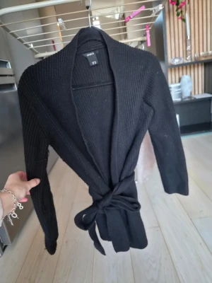 Svart ribbstickad kofta från Lindex - Svart ribbstickad kofta från Lindex med knytskärp i midjan. Det är storlek xs