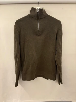 Olivgrön stickad tröja med halvzip Jack and Jones  - Snygg olivgrön stickad tröja med hög krage och halv dragkedja framtill. Tröjan har lång ärm och är tillverkad i ett mjukt, ribbstickat material. Perfekt för lager-på-lager och enkel att matcha med jeans. Helt oanvänd på grund av fel storlek. Pris kan diskuteras!