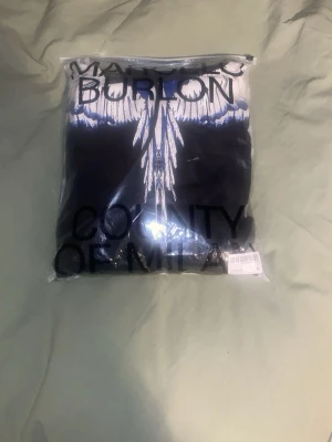 Marcelo Burlon svart hoodie med vingar - Svart hoodie från Marcelo Burlon med ikoniskt vingtryck i vitt och blått över axlarna. Klassisk känguruficka framtill och justerbar huva. Perfekt statement-plagg för dig som vill sticka ut med streetwear-vibe.