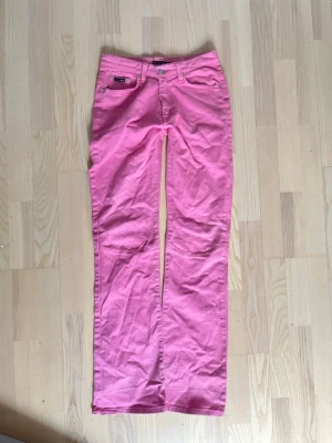 Rosa lågmidjade jeans - Säljer ett par snygga rosa bootcut jeans med klassisk femficksdesign och hällor för bälte. Jeansen har en normal passform och är perfekta för dig som vill sticka ut med färg. 