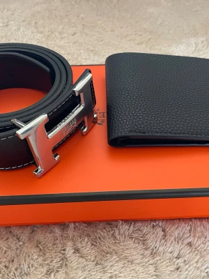 Svart skärp med silverdetaljer - Snyggt svart skärp med klassiskt H-spänne i silverfärg. Skärpet är gjort i exklusivt skinn med vit kontrastsöm och har en stilren, tidlös design. Perfekt accessoar för att lyfta din outfit. Allt är i original förpackning och skärpet är 110 cm. Priset går att diskuteras!