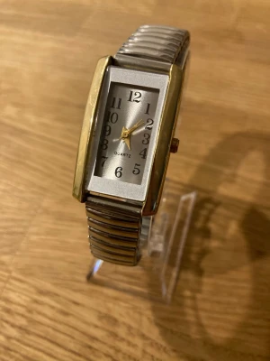 Vintage Ladies Rectangle Gold Flexband Watch - Klocka med rektangulär guldfärgad boett och silverfärgat flexibelt armband. Urtavlan är silverfärgad med svarta arabiska siffror och guldfärgade visare. Klockan har ett quartz-urverk. Fint skick enligt bilder, behöver bara nytt batteri.  Begagnat värde: < 500 SEK Mitt pris: 189 SEK  Skickas alltid snabbt och spårbart. Skriv vid frågor och se gärna mina andra annonser!   GRATIS: För återkommande kunder erbjuder jag personlig experthjälp för dig att göra nya fynd (nytt & begagnat). Fråga för mer i