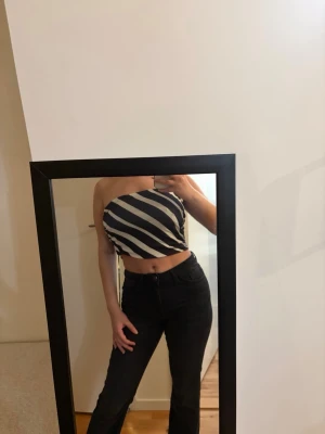 Randig tubtopp från H&M - Snygg tubtopp från H&M i svart och vitt med diagonala ränder. Toppen är axelbandslös och sitter tight runt överkroppen, perfekt för en trendig och avslappnad stil. Materialet är mjukt och stretchigt för en bekväm passform.