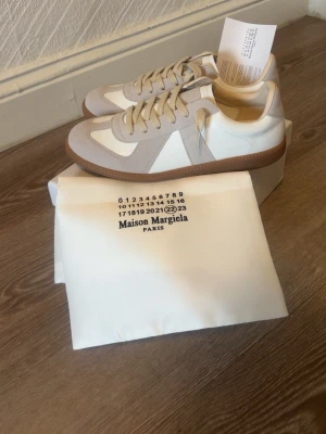 Maison margiellas - sneakers i vitt och beige läder och mocka med klassisk gummisula. Snygg retrostil med låga snitt och neutrala färger som passar till det mesta. Ikonisk design med diskreta detaljer och sköna material.