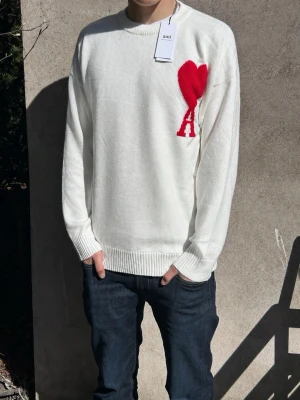 Vit stickad tröja från Ami Paris - Vit Ami Paris tröja med rött hjärta på bröstet. Helt ny med tags kvar. Storlek M och riktigt skön passform. Enkel att styla med jeans eller cargos.