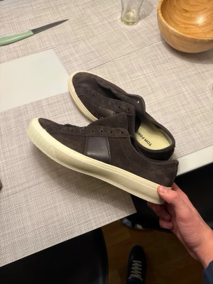 Tom ford skor  - Snygga bruna sneakers från Tom Ford i mocka med detaljer i läder och vit sula. Klassisk låg modell med stilren design och diskreta sömmar. Perfekta för dig som gillar en clean och tidlös look.