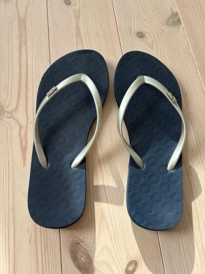 Blå/ silver flip-flops från Roxy storlek 36 - Snygga blå/ silver färgade flip flops från Roxy. Perfekta för sommaren och strandhäng. Tillverkade i mjukt och flexibelt material för skön komfort hela dagen. Storlek 36