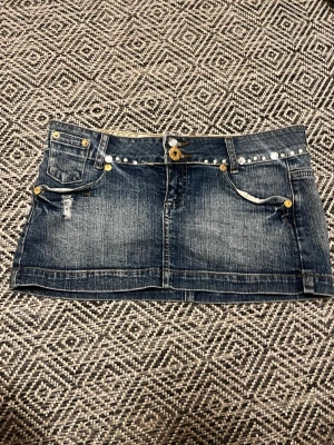 Mörkblå jeanskjol med nitar - Jättefin kjol! Detaljerna är egengjorda. Midjemått 41 cm och längd 26-27 cm.