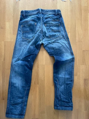 Diesel raka jeans med slitningar - Snygga blå jeans med raka ben och klassisk femficksdesign. Jeansen har slitna detaljer och ljusare partier för en cool, avslappnad look. Tillverkade i denim med synliga sömmar och knappgylf. Perfekta för en trendig vardagsstil. Längd 100, midja 40. Defekt på sista bilden.