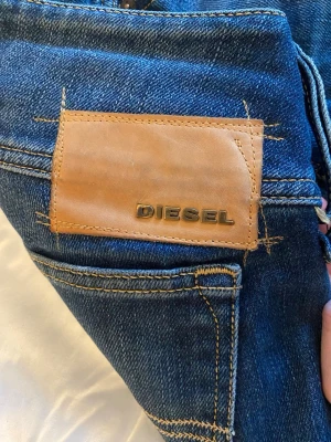 Blå jeans från Diesel Cherock - Säljer ett par klassiska blå jeans från Diesel, modell Cherock. Jeansen har en snygg tvätt, raka ben och detaljer i kontrastsömmar. Tillverkade i slitstark denim med läderpatch bak i midjan. Perfekta för en cool och avslappnad stil. Men lite söndriga till fötterna men annars helt nya.
