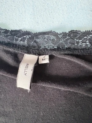 Svart omlottopp med spets från Nelly - Snygg svart omlottopp från Nelly med v-ringning och spetsdetaljer längs halsringningen 