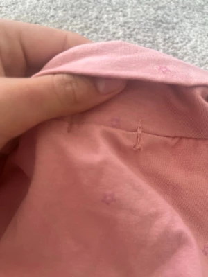 Rosa polotopp med små stjärnor - En rosa polotopp med lång ärm och små lila stjärnor som mönster. Toppens material är mjuk bomull och den har en klassisk polokrage. Perfekt för dig som gillar en enkel men söt stil.